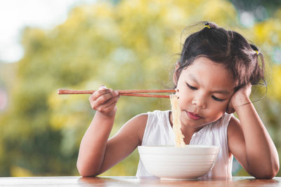 Cute girl eating noodles at table in public park