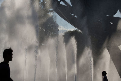 Silhouette people by fountain against sky