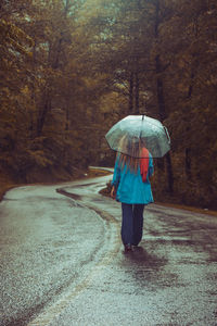 Rear view of woman with umbrella walking on road during rainy season