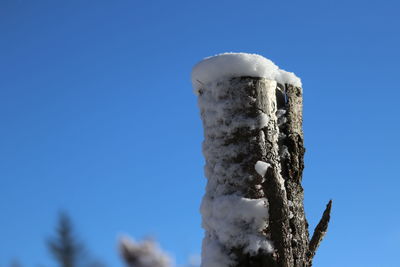 Close-up of frozen wooden post against sky during winter