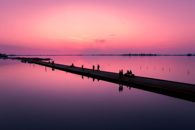 Silhouette people by lake against dramatic sky during sunset