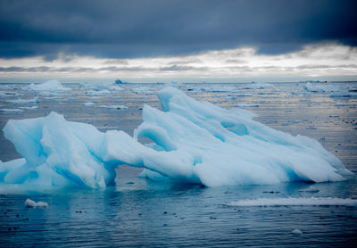 Icebergs in sea against cloudy sky during winter