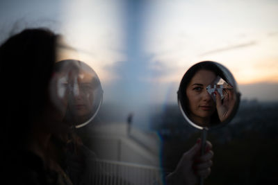 Portrait of young woman holding sunglasses against sky