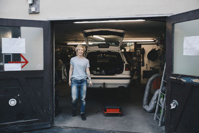 Full length portrait of happy owner at entrance of auto repair shop