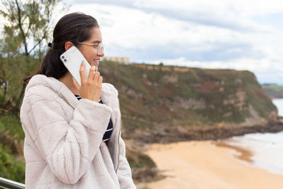 Young ethnic woman talking on smartphone near sandy beach