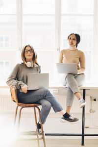 Portrait of female computer programmers with laptops sitting at desk in office