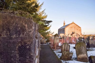 Tombstones in cemetery by church against clear sky