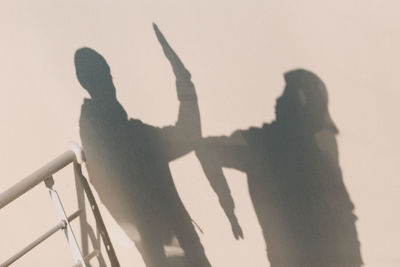 Shadow of people on wall against clear sky