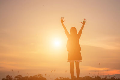 Rear view of silhouette woman standing against sky during sunset