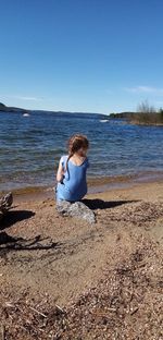 Rear view of boy sitting on shore at beach against sky