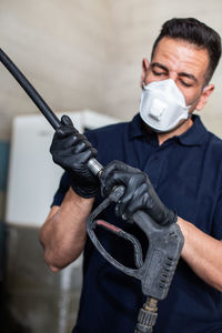 Adult man in respirator and latex gloves attaching nozzle to hose while working in garage