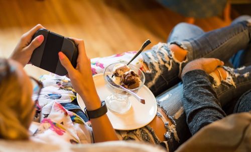 Woman with ice cream playing video game by man on sofa at home