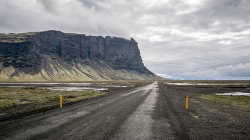 Road by cliff against cloudy sky