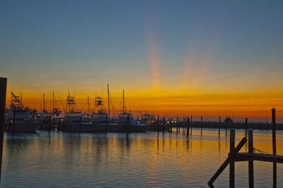 Sailboats moored at harbor against sky during sunset