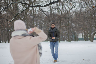 Couple playing on snow filed against bare trees