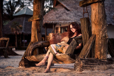 Woman reading book while sitting on wooden bench