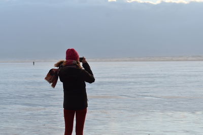 Rear view of woman photographing frozen lake