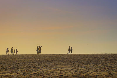 Silhouette people on beach against clear sky during sunset