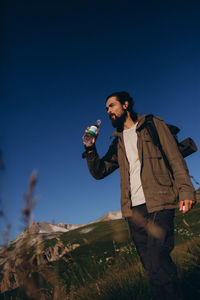 Full length of man drinking coffee on field against clear blue sky