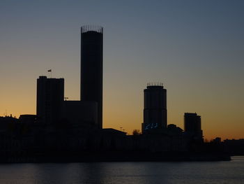 Buildings by river against sky during sunset