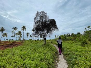 Rear view of woman walking on field against sky