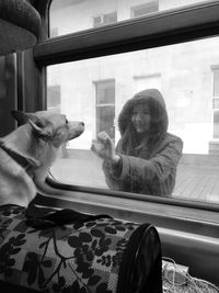 Young woman looking at dog through window of train