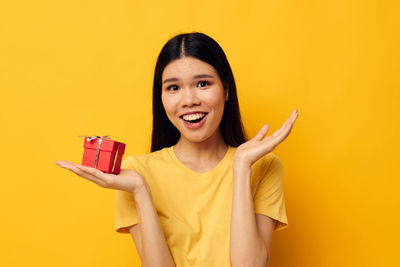 Young woman holding mobile phone against yellow background