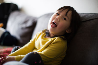 Portrait of cute girl with mouth open sitting on sofa at home