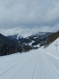 Snow covered landscape against cloudy sky