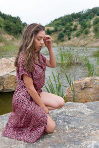 Beautiful young woman sitting by lake