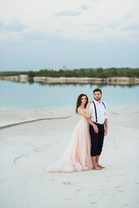 Full length of woman with arms raised while standing on shore against sky