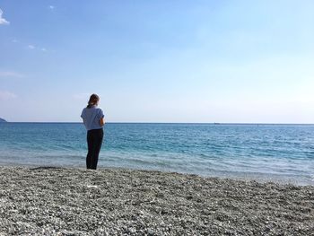 Rear view of man standing on beach against clear sky