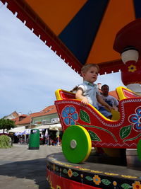 Boy and man in amusement park against sky