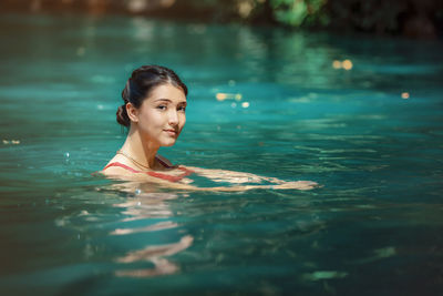 Young latina woman standing and looking at camera, in blue green waters of rio blanco in costa rica