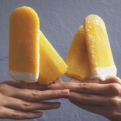 Cropped image of hand holding ice creams against wall