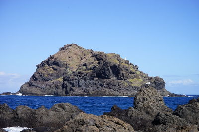 Rock formations on shore against clear blue sky