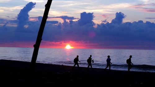 Silhouette people standing on beach against sky during sunset