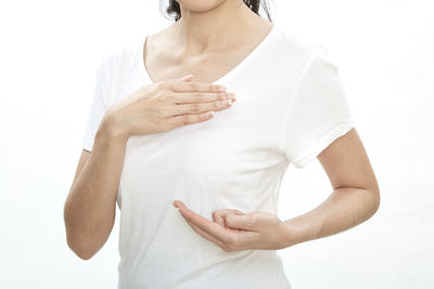 Midsection of woman touching breast against white background