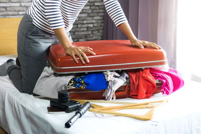 Low section of woman packing suitcase on bed at home