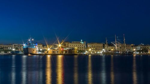 Illuminated buildings by sea against clear sky at night