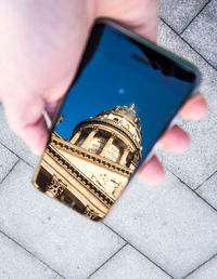 Cropped hand holding smart phone with reflection of church