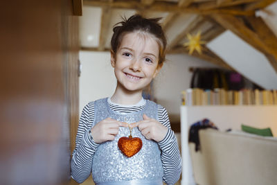 Smiling girl holding heart shape decoration at home