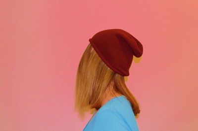 Side view of woman wearing knit hat against coral background