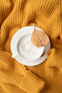 Cup of cappuccino coffee on yellow sweater top view flat lay