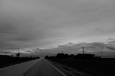 Road amidst field against sky at dusk