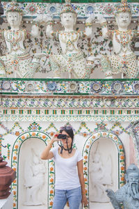 Asian woman in a white t-shirt taking a photo directly aimed at the viewer at temple in asia