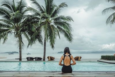 Rear view of woman standing by swimming pool against sky