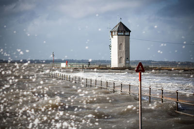 Lighthouse on beach by sea against sky