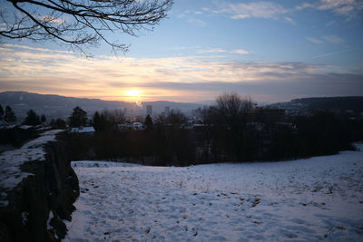 Snow covered field against sky during sunset