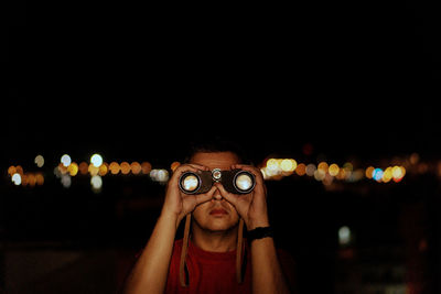 Mature man looking through binoculars while standing against clear sky at night